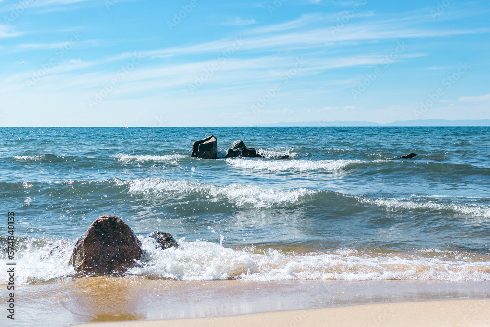 Fototapeta premium Two groups of stones are washed by the waves of Lake Baikal at summer sunny day, beautiful scenic blue seascape