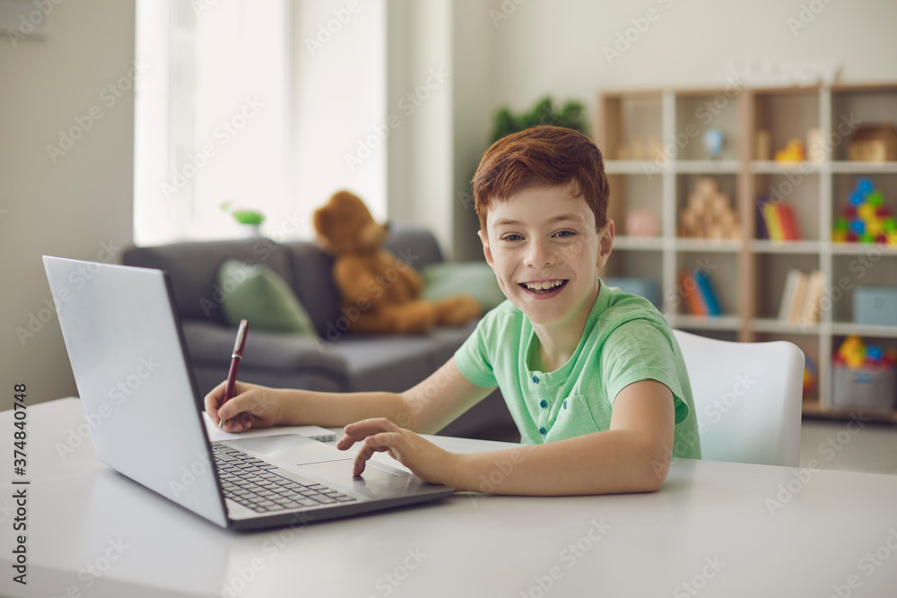 Schoolboy boy sitting at a desk with a laptop, writes school lessons during homework. Schoolboy boy sitting at a desk with a laptop, writes school lessons during homework.