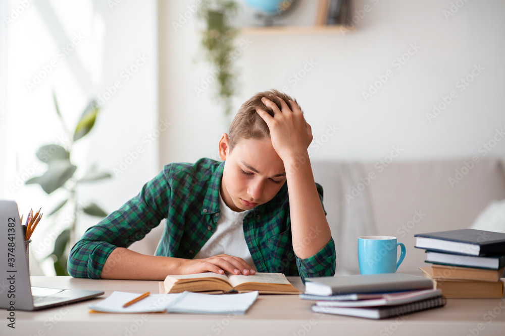 Exhausted schooler sitting at desk in his room, studying Exhausted schooler sitting at desk in his room, studying