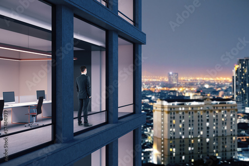 Young businessman standing in office and looking on night city.