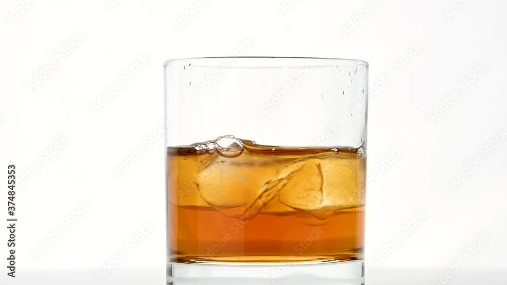 Ice cubes spin in glass of whiskey over white Ice cubes spin in glass of whiskey over white
