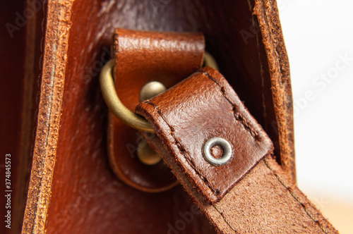 Fashionable brown women's bag made of genuine leather close-up. Fashion concept. Details of leather bag, belt, metal buckle, clasp, thread stitching, macro shot. Stylish female accessory