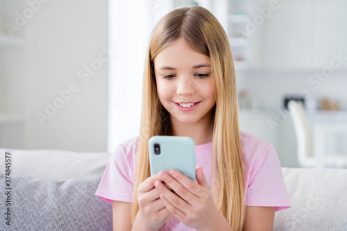 Close up photo of positive small kid girl study remote rest relax use smartphone follow share repost quarantine stay home information sit comfort couch in house indoors
