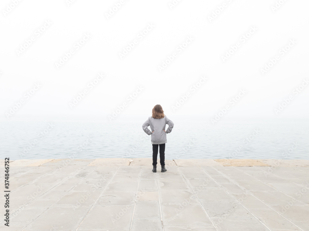Girl child looking at grey distant horizon on a ocean foggy day. Girl child looking at grey distant horizon on a ocean foggy day.