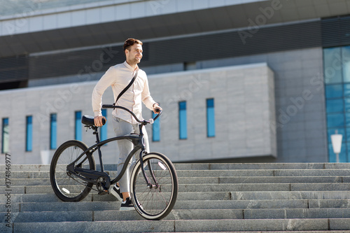 Businessman holds bicycle in his hands and looking away, goes on stairs