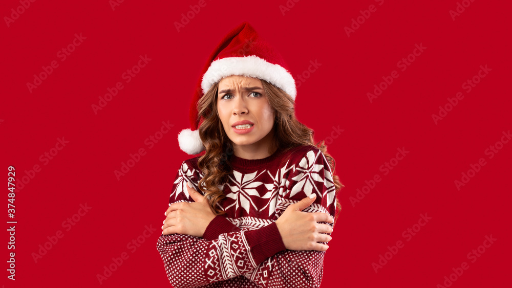 Unhappy young girl in Christmas outfit shivering from cold over red background Unhappy young girl in Christmas outfit shivering from cold over red background