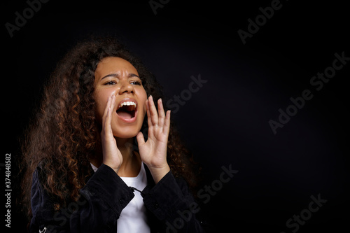 Portrait of young beautiful black woman standing in the dark showing emotions. Female with emotional facial expression over black wall background. Close up, copy space.