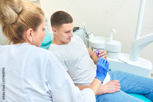 woman doctor dentist shows a mouth guard to a man. the patient sits in the dental chair in the office