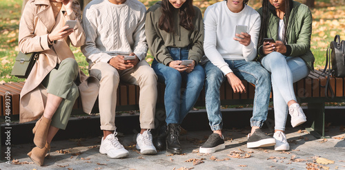 Tableau sur toile Group of international teenagers using smartphones at park