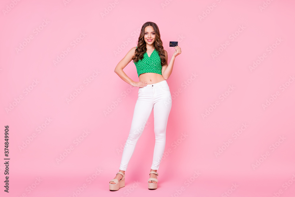 Full size photo of positive girl hold credit card easy online internet paying wear green dotted crop singlet white trousers isolated over pastel color background Full size photo of positive girl hold credit card easy online internet paying wear green dotted crop singlet white trousers isolated over pastel color background