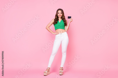Full size photo of positive girl hold credit card easy online internet paying wear green dotted crop singlet white trousers isolated over pastel color background