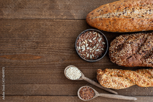 The bakery, several different fresh loaves of bread with a crisp crust, sprinkled with seeds and sesame seeds on a wooden background with boils of wheat.