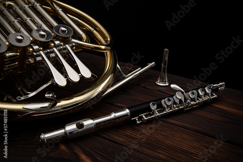 Two musical instruments French horn and flute on a wooden surface on a black background