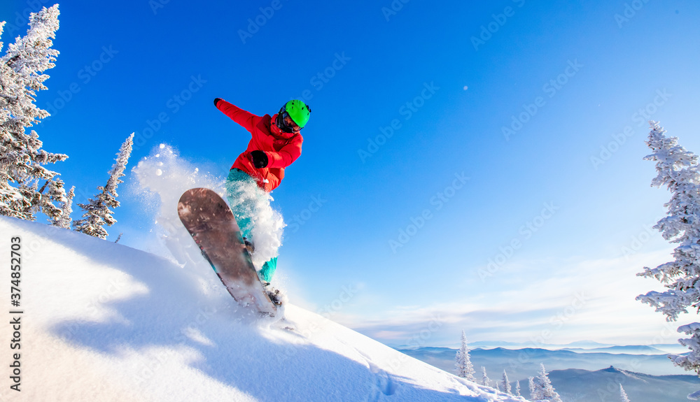 Snowboarder jumping through air with deep blue sky in background, Freeride winter forest