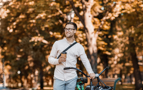 Modern lifestyle and ecological transport. Happy hipster holding coffee and walking with bike