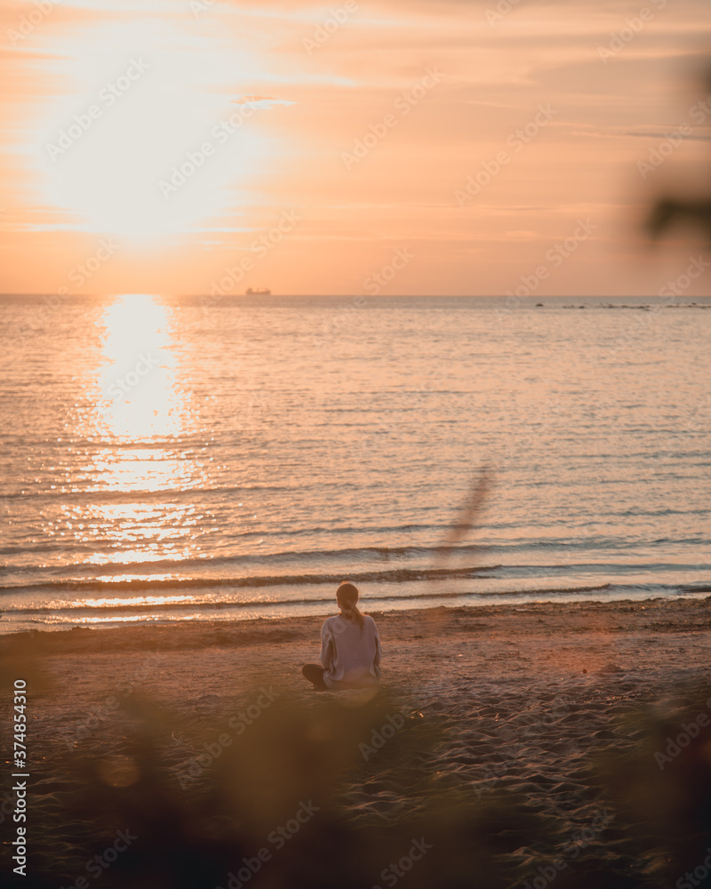 Girl sitting at sunset by the sea and meditating