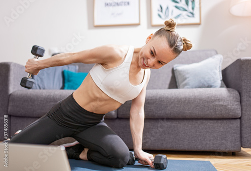 Cheerful female exercising with dumbbells near laptop