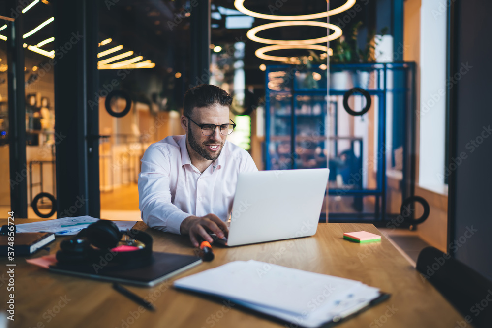 Fototapeta premium Positive male worker working on laptop in modern office