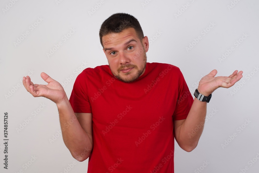 Young caucasian man wearing red t-shirt over white background, shrugs shoulders with hesitation, faces doubtful situation, spreads palms, Hard decision Young caucasian man wearing red t-shirt over white background, shrugs shoulders with hesitation, faces doubtful situation, spreads palms, Hard decision