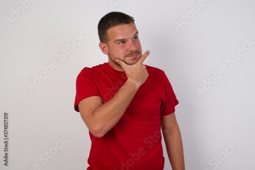 Young caucasian man wearing red t-shirt over white background Thinking worried about a question, concerned and nervous with hand on chin.