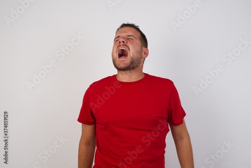 Young beautiful caucasian man with short hair wearing red casual shirt angry and mad screaming frustrated and furious, shouting with anger. Rage and aggressive concept.