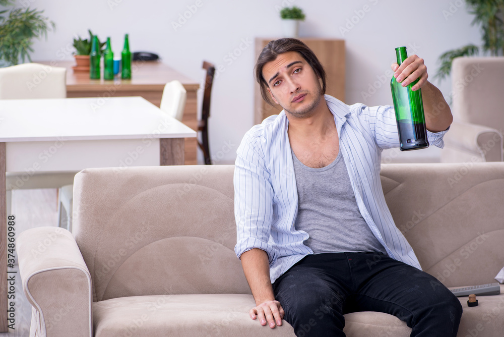Young male alcoholic drinking wine at home