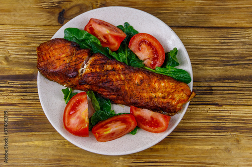 Grilled salmon fillet with spinach and tomatoes on wooden table. Top view