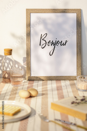 Stylish interior of kitchen space with wooden table, brown mock up photo frame, beige tablecloth, food and kitchen accessories. Country side mood. Summer vibe.