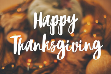 Happy Thanksgiving greeting card. Hand written Happy Thanksgiving text on blurred background of pumpkin, autumn leaves, warm lights on yellow knitted sweater.