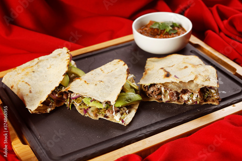 Traditional Oaxacan tlayuda stuffed with meat, melted cheese and avocado, accompanied by red chili sauce.