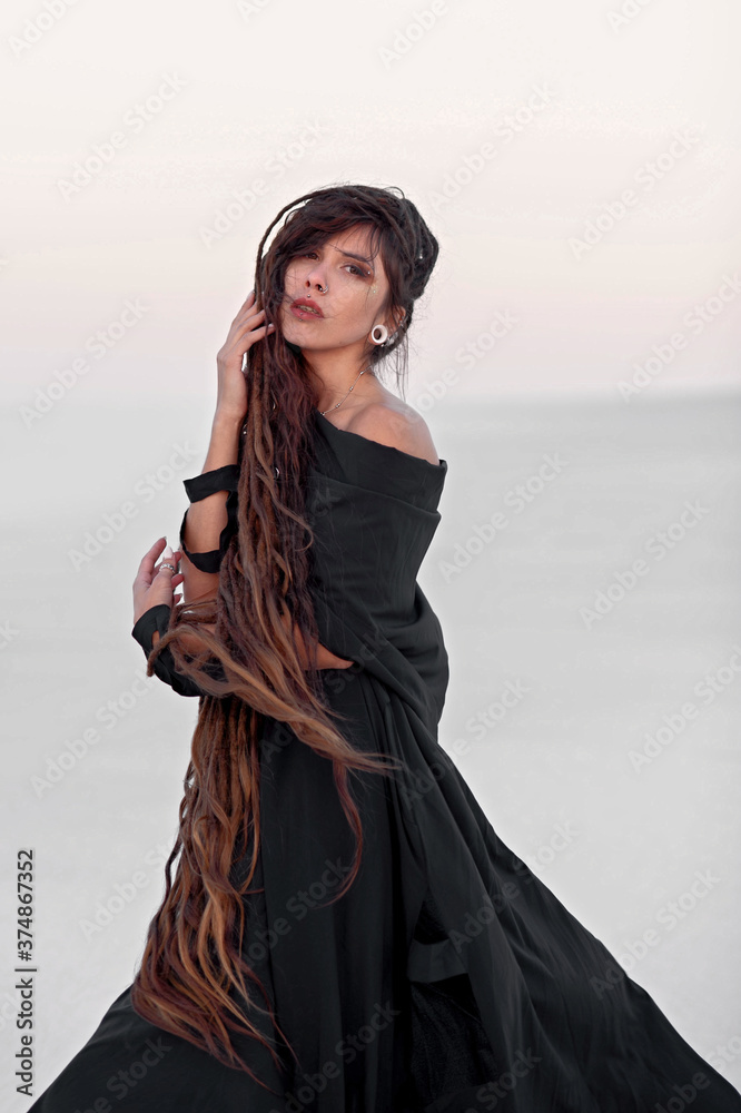 Naklejka premium Girl with dreadlocks in a dress in the desert on white sand. Sunset