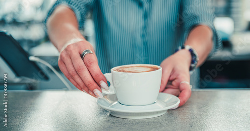 Closeup female barista hands holding cup of aromatic latte or cappuccino coffee in bar or cafe