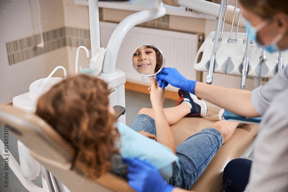 Cute boy sitting in dental chair and looking in the mirror Cute boy sitting in dental chair and looking in the mirror