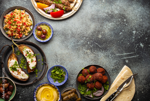 Middle eastern or Mediterranean dinner with grilled kebab, falafel, roasted and fresh vegetables, assorted Arabic meze and appetizers on rustic background table. Dinner table overhead, space for text 