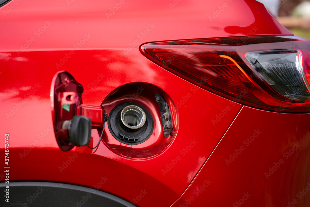 An open fuel tank cap of a red car for filling gasoline or diesel fuel into the gas tank. The back of the car with an open gas tank.