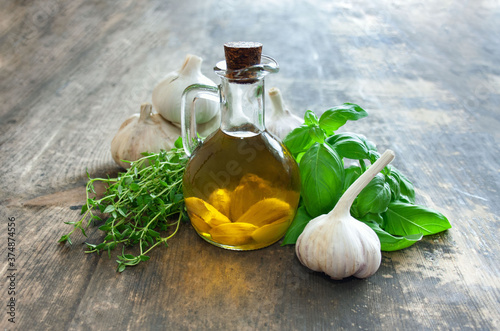 Olive oil with garlic in a jug, next to the basil, thyme and garlic