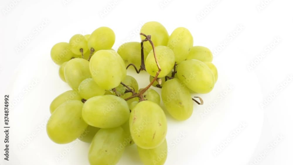Ripe juicy grapes rotate on a plate. Close-up of a bunch of white grapes. Fresh bunch of juicy grapes rotate on a white background. Ripe juicy grapes rotate on a plate. Close-up of a bunch of white grapes. Fresh bunch of juicy grapes rotate on a white background.