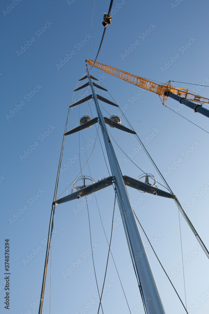 Placing a mast on a super sailing yacht at the harbor. Ship building industry. Shipyard. Building superyachts. Rigging. Crane. Placing a mast on a super sailing yacht at the harbor. Ship building industry. Shipyard. Building superyachts. Rigging. Crane.