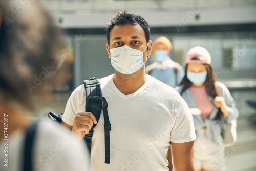 Handsome male in protective mask traveling in line through an airport