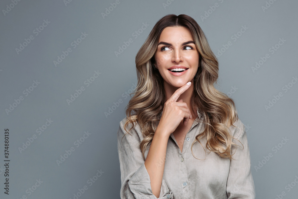 Blonde woman with curly hair dressed in linen shirt, smiles pleasantly, looking at blank space, happy with discounts and sales, arm on chin, isolated on grey background. Advertising service, low price Blonde woman with curly hair dressed in linen shirt, smiles pleasantly, looking at blank space, happy with discounts and sales, arm on chin, isolated on grey background. Advertising service, low price