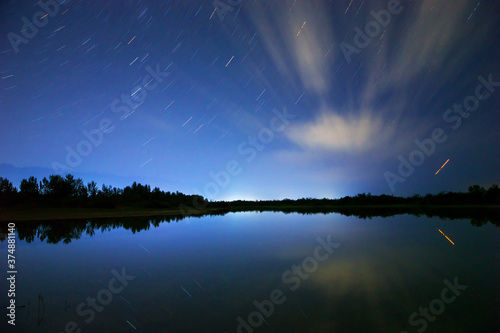 Starry sky and clouds. Night landscape, lights reflecting in the sea and mountains. Natural background