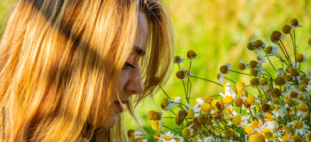 Naklejka premium Young beautiful smiling woman smells bouquet of yellow field flowers, against green summer fiel.