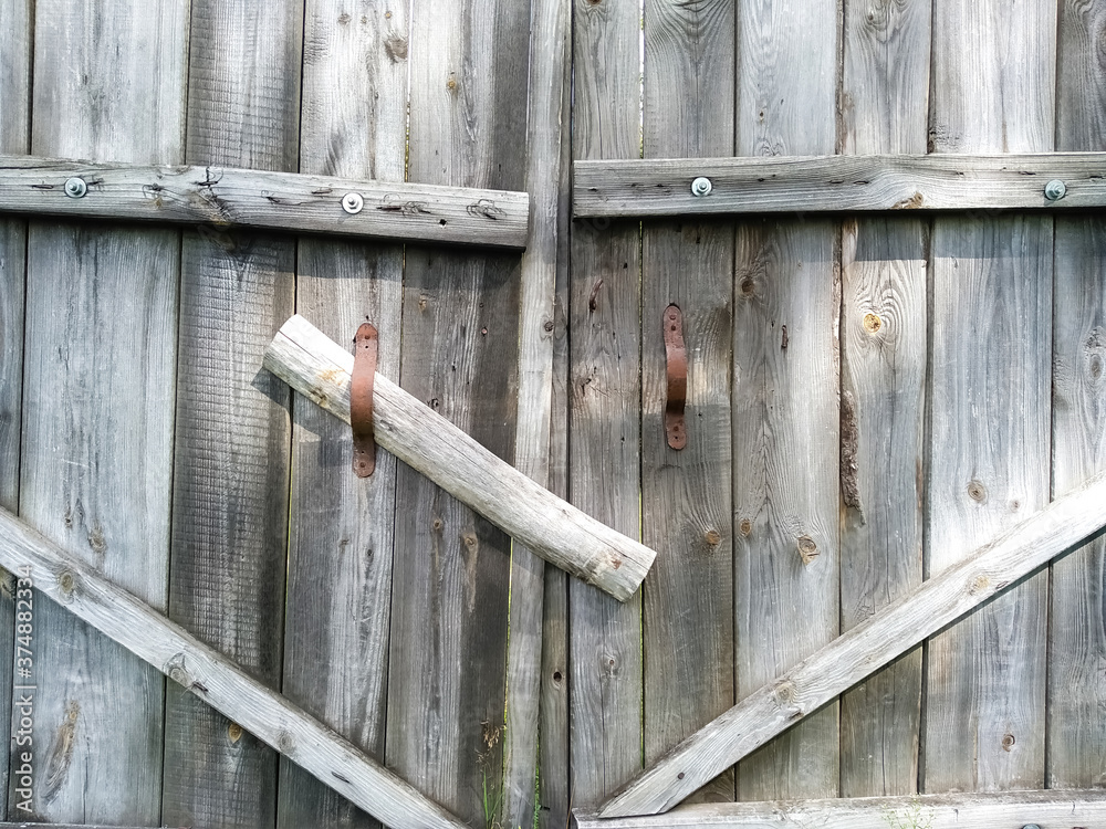 Close-up old wooden rickety gates. Rustic gate made of dry gray planks with rusty handles. Countryside scene. Fragment of closed wooden gate. Close-up old wooden rickety gates. Rustic gate made of dry gray planks with rusty handles. Countryside scene. Fragment of closed wooden gate.