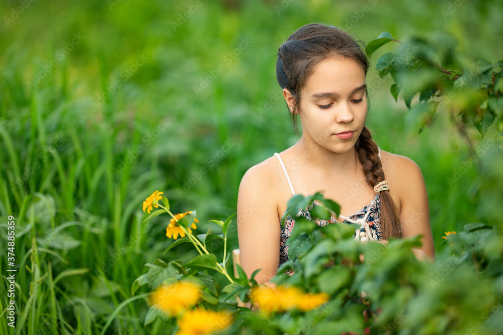Selective focus of young caucasian female teenager with brown braid sitting on wooden chair in garden near bush and flowers. Front view of farm girl collecting harvest in countryside. Selective focus of young caucasian female teenager with brown braid sitting on wooden chair in garden near bush and flowers. Front view of farm girl collecting harvest in countryside.