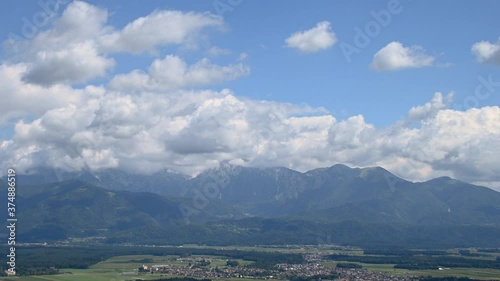 Time lapse white puffy clouds rolling over Alps mountains in Slovenia. Ljubljana basin with villages in foreground. Elevated aerial view. Wide shot, left truck parallel moving photo