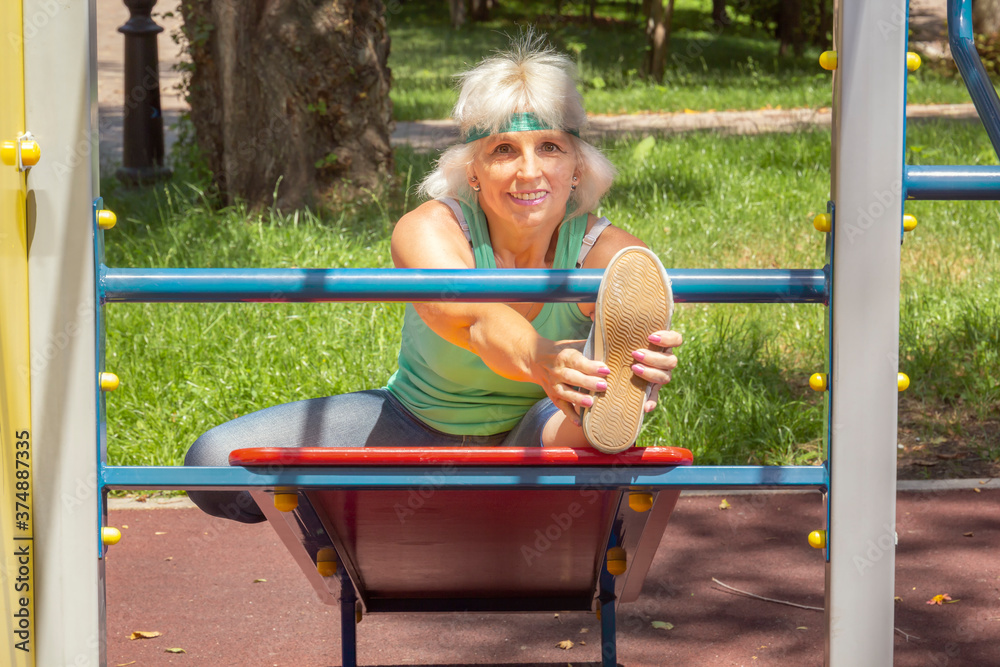 Obraz premium Slender elderly woman with gray hair conducts individual fitness classes on a simulator in a city park. Close-up