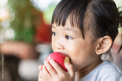 Portrait​ image​ of​ 1-2​ yeas​ old​ of​ baby.​ Happy​ Asian child girl eating and biting an red apple. Enjoy eating moment. Healthy food and kid concept.​ Vintage​ style.