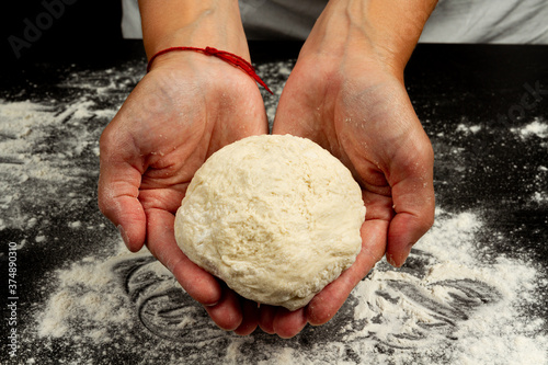 girl chef making homemade fresh yeast dough for making pizza on black wooden table background