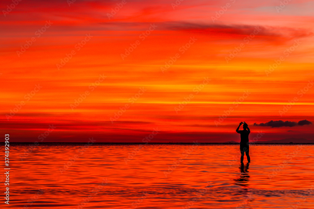 Silhouette of a man taking a photo of a vivid sunset