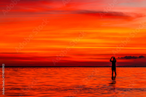 Fototapeta Naklejka Na Ścianę i Meble -  Silhouette of a man taking a photo of a vivid sunset